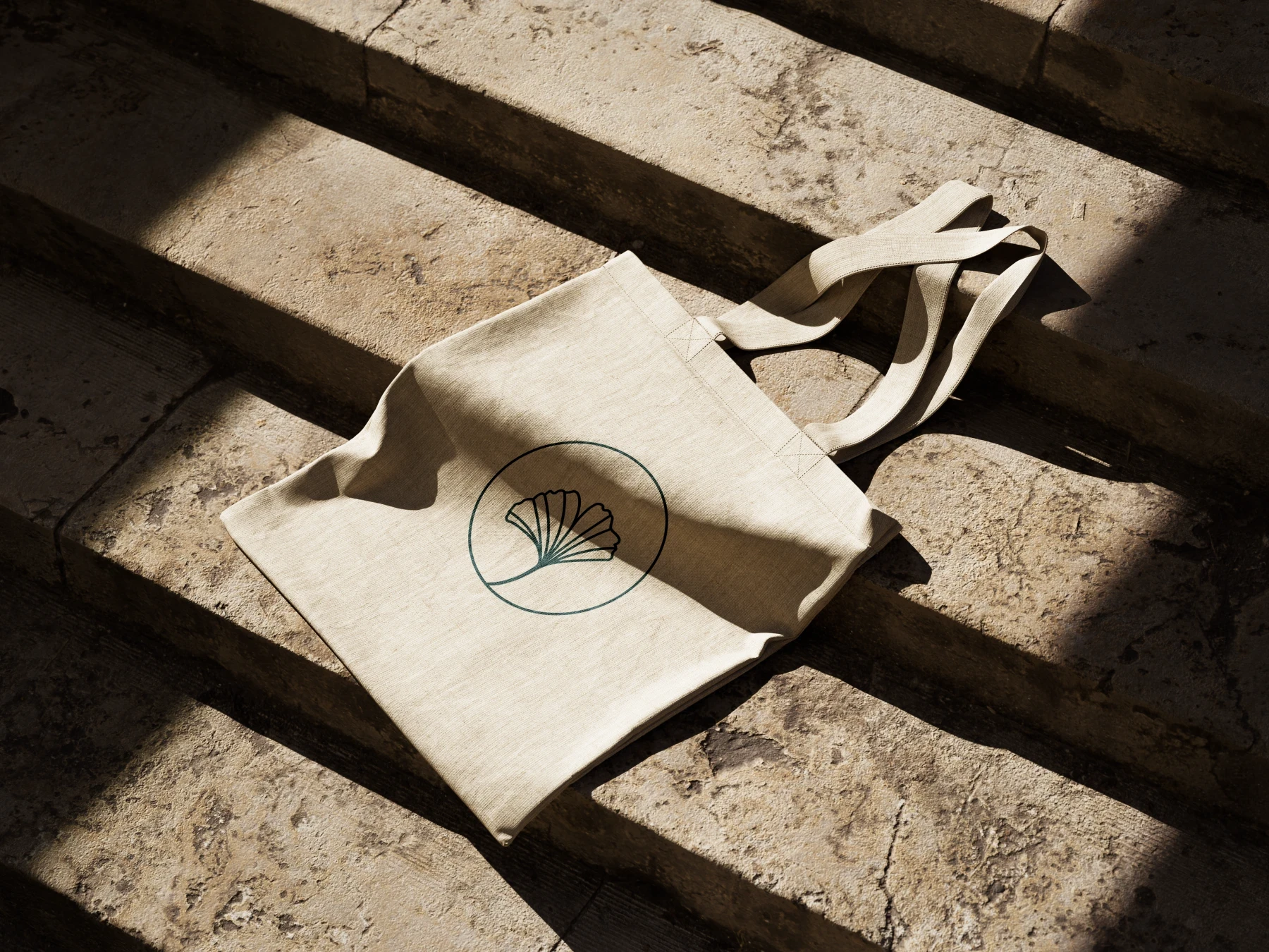 Tote bag en toile naturelle avec le symbole de feuille de Pigment It Pottery, posé au soleil.